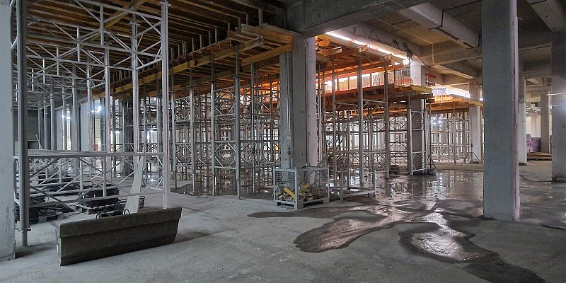 Deckenschalung mit Traggerüst in einem Rohbau, nasser Betonboden im Vordergrund