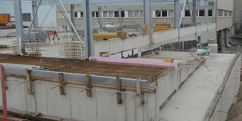 Stahlkonstruktion auf Betonfundament in einem Industrie-Neubau, mit Schalung und Bewehrung im Vordergrund